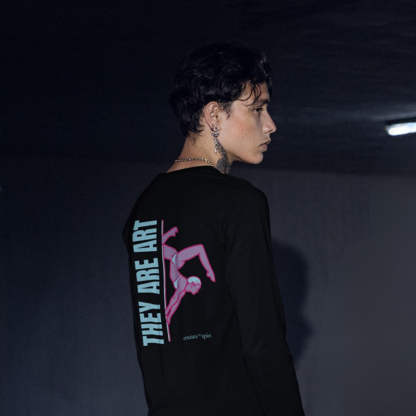 Person wearing a black long-sleeve shirt with a graphic design saying "They Are Art" on the back against a dark background