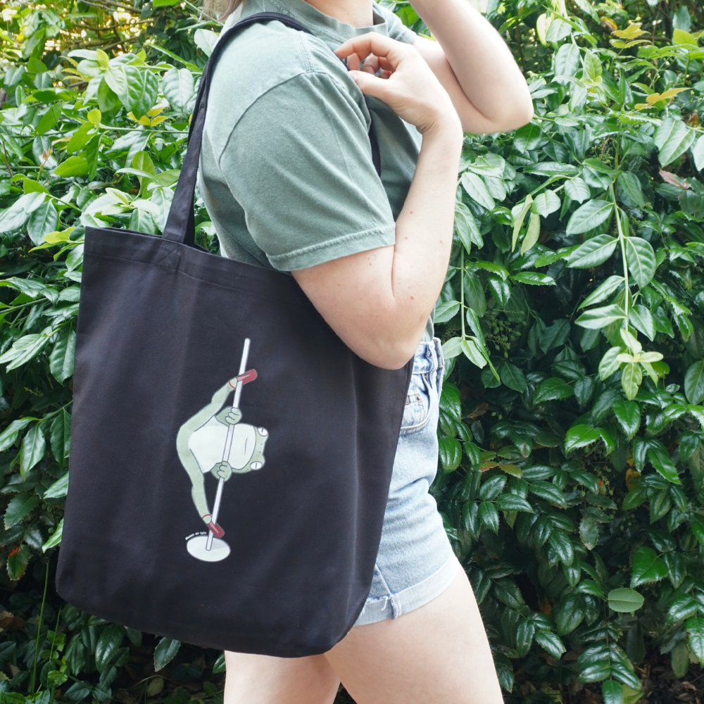 Woman holding a black tote bag with a dancing frog on the front.