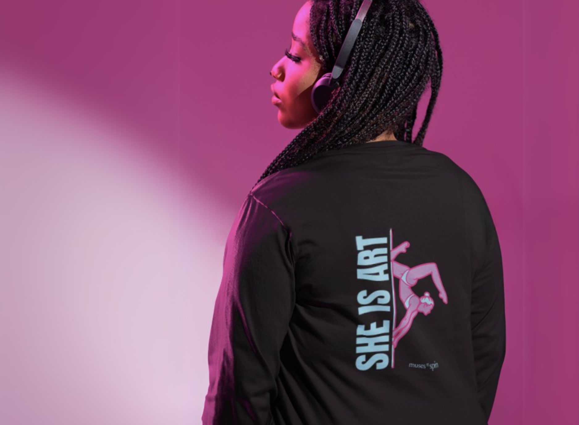 Woman facing a pink background, wearing a black long-sleeve shirt with a design saying 