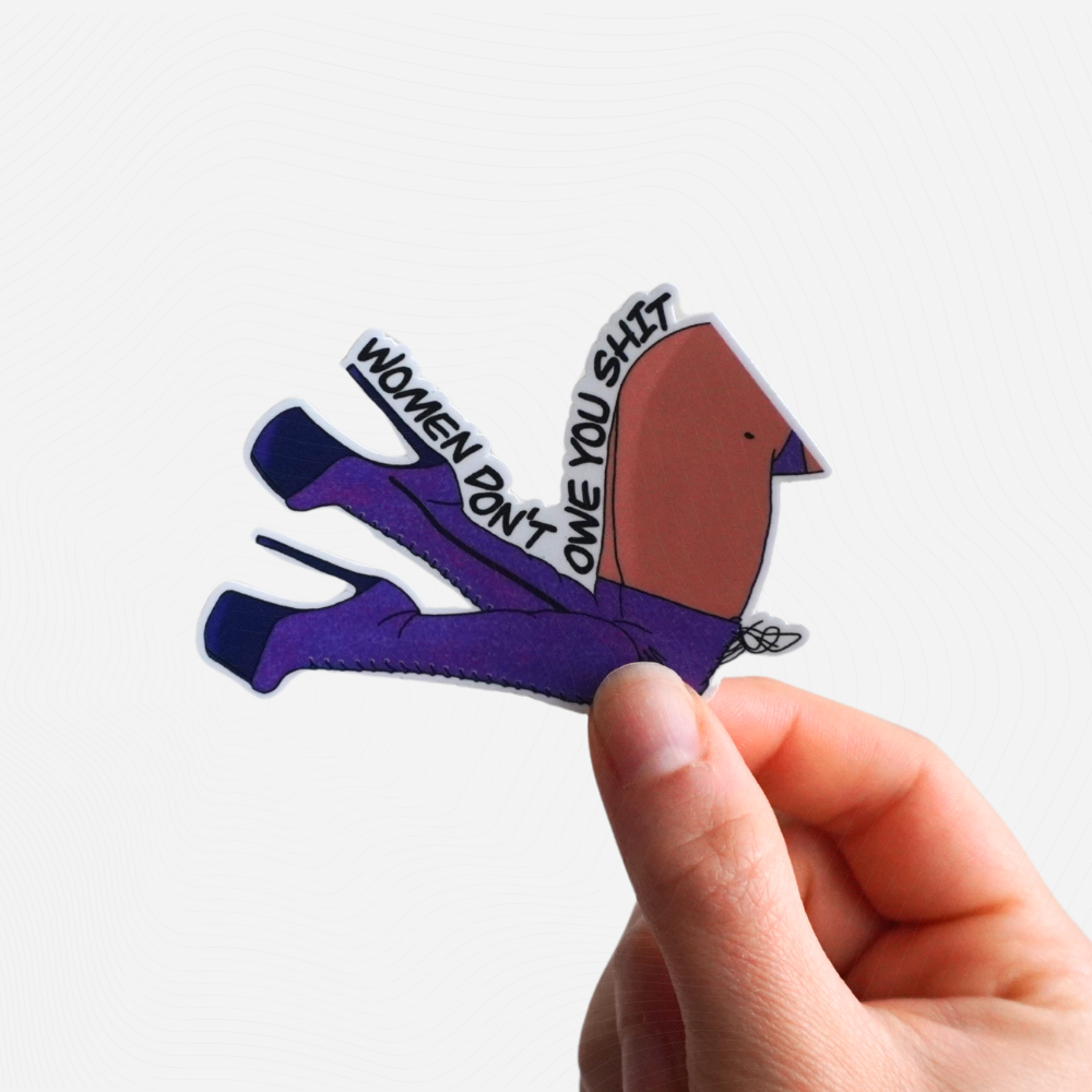 Sticker of a high-heeled shoe with "Women Don't Owe You Shit" text held by a hand on a white background