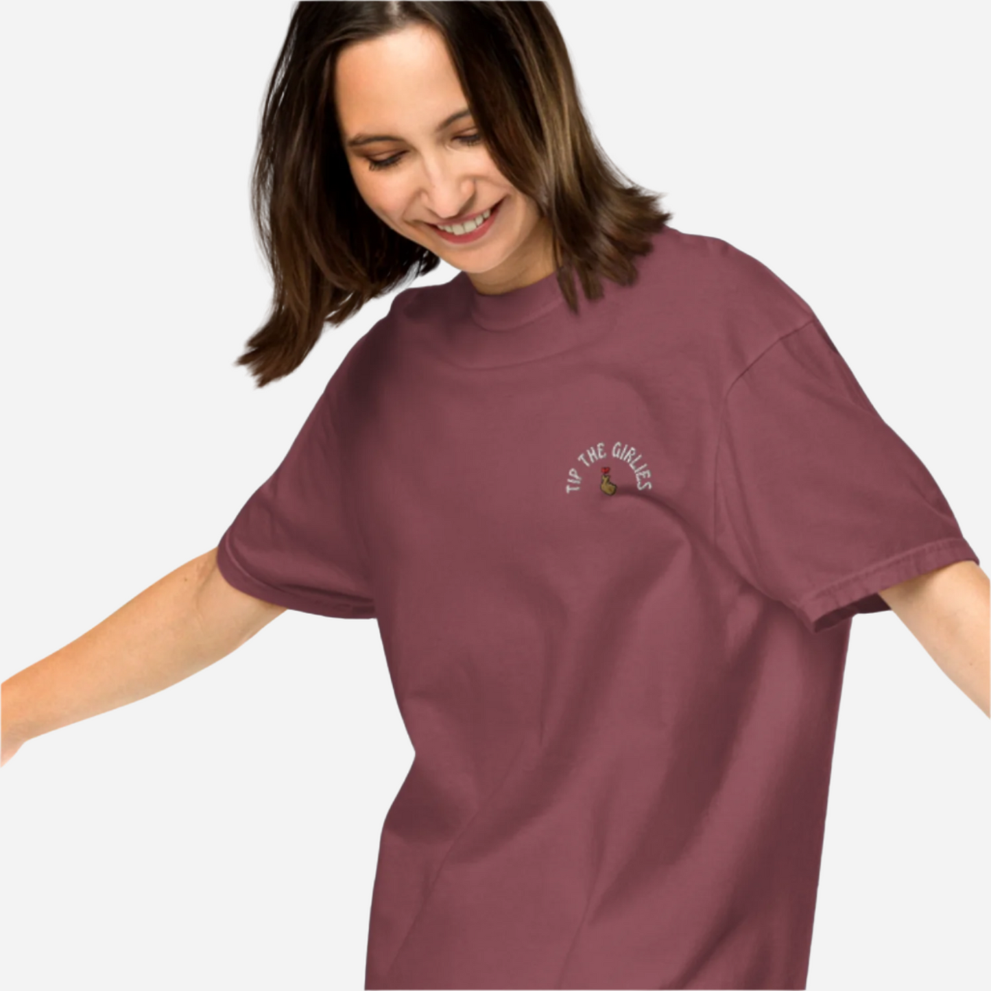 Woman in front of a white background wearing a loose maroon tshirt with the words "Tip the Girlies" embroidered on the left chest area.