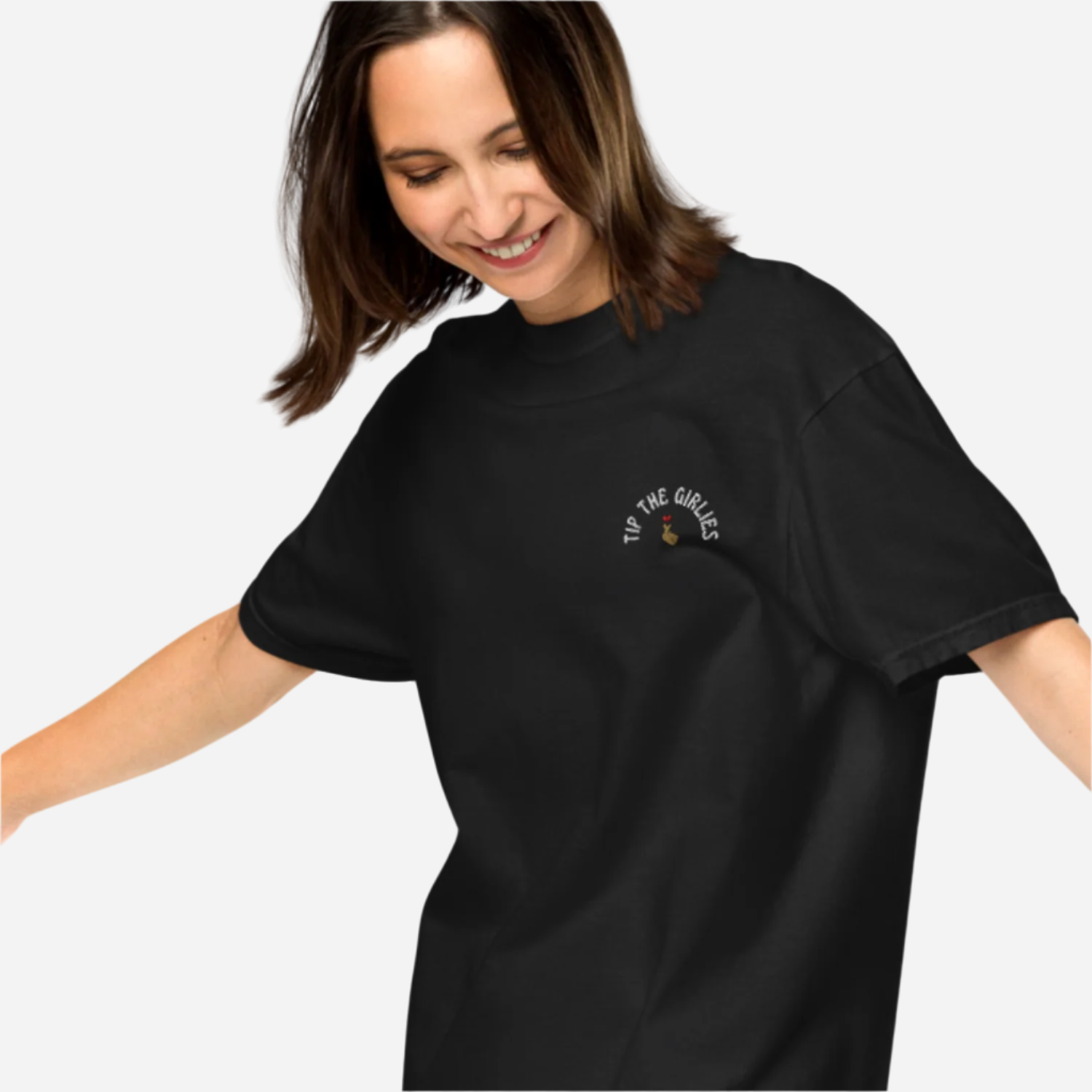 Woman in front of a white background wearing a loose black tshirt with the words "Tip the Girlies" embroidered on the left chest area.