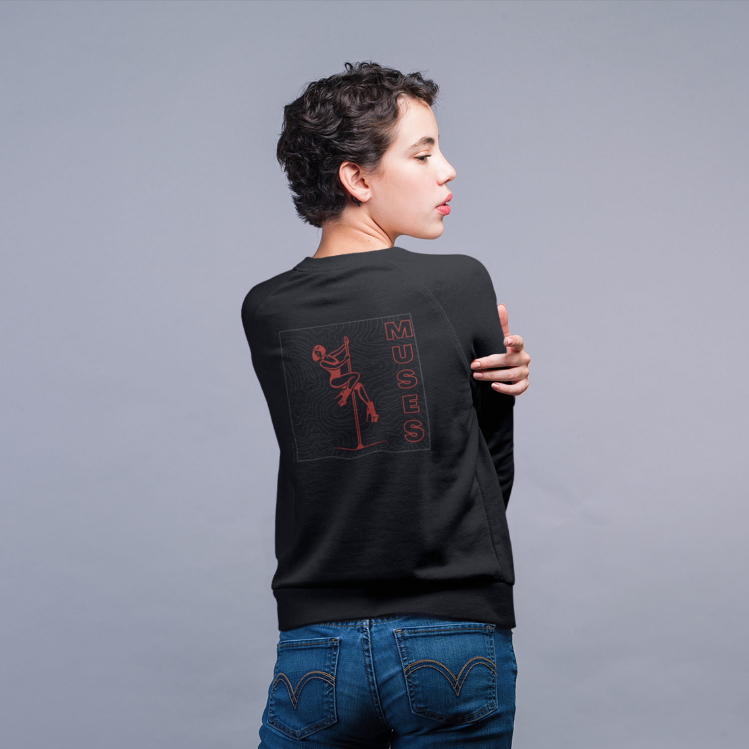 Woman in front of a grey background wearing a black sweater with a dark red and grey design of a pole dancer and the word 