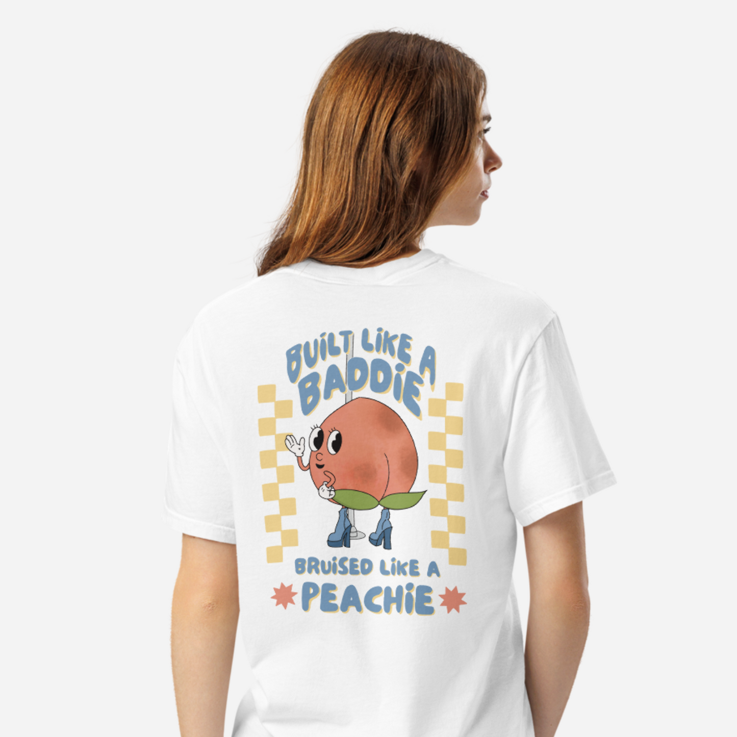 Woman facing the back wearing a white tshirt with a graphic of a cartoon peach. It says "Built like a baddie, bruised like a peachie"