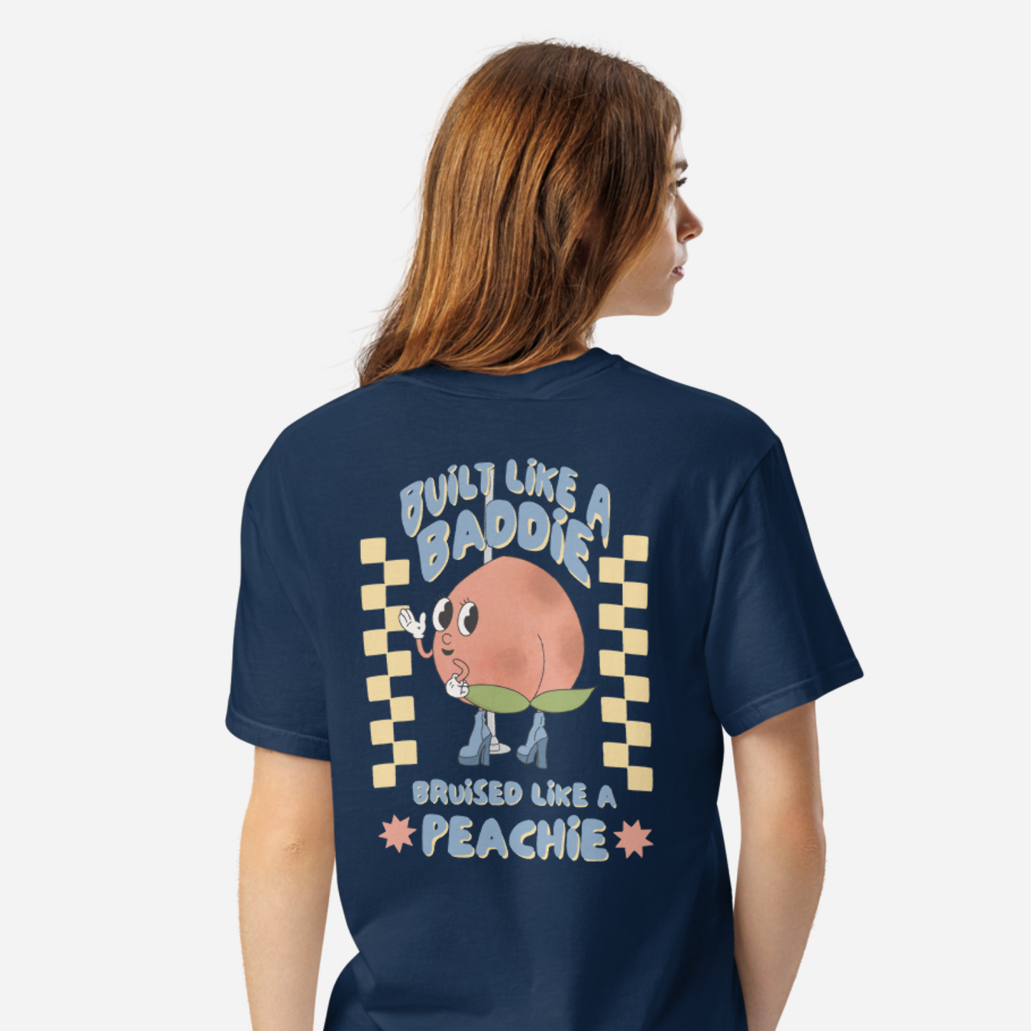 Woman facing the back wearing a navy tshirt with a graphic of a cartoon peach. It says "Built like a baddie, bruised like a peachie"