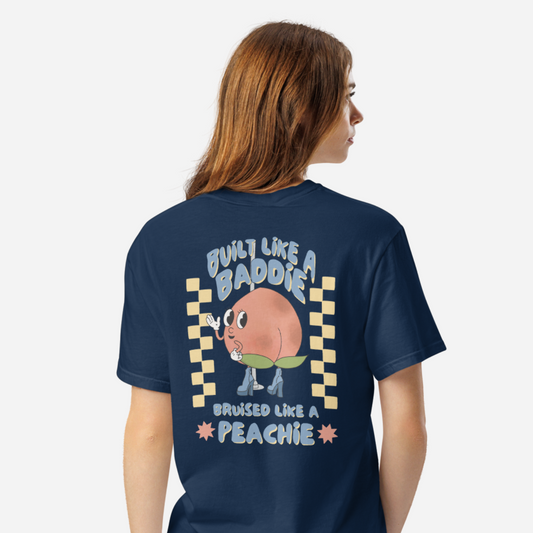 Woman facing the back wearing a navy tshirt with a graphic of a cartoon peach. It says "Built like a baddie, bruised like a peachie"