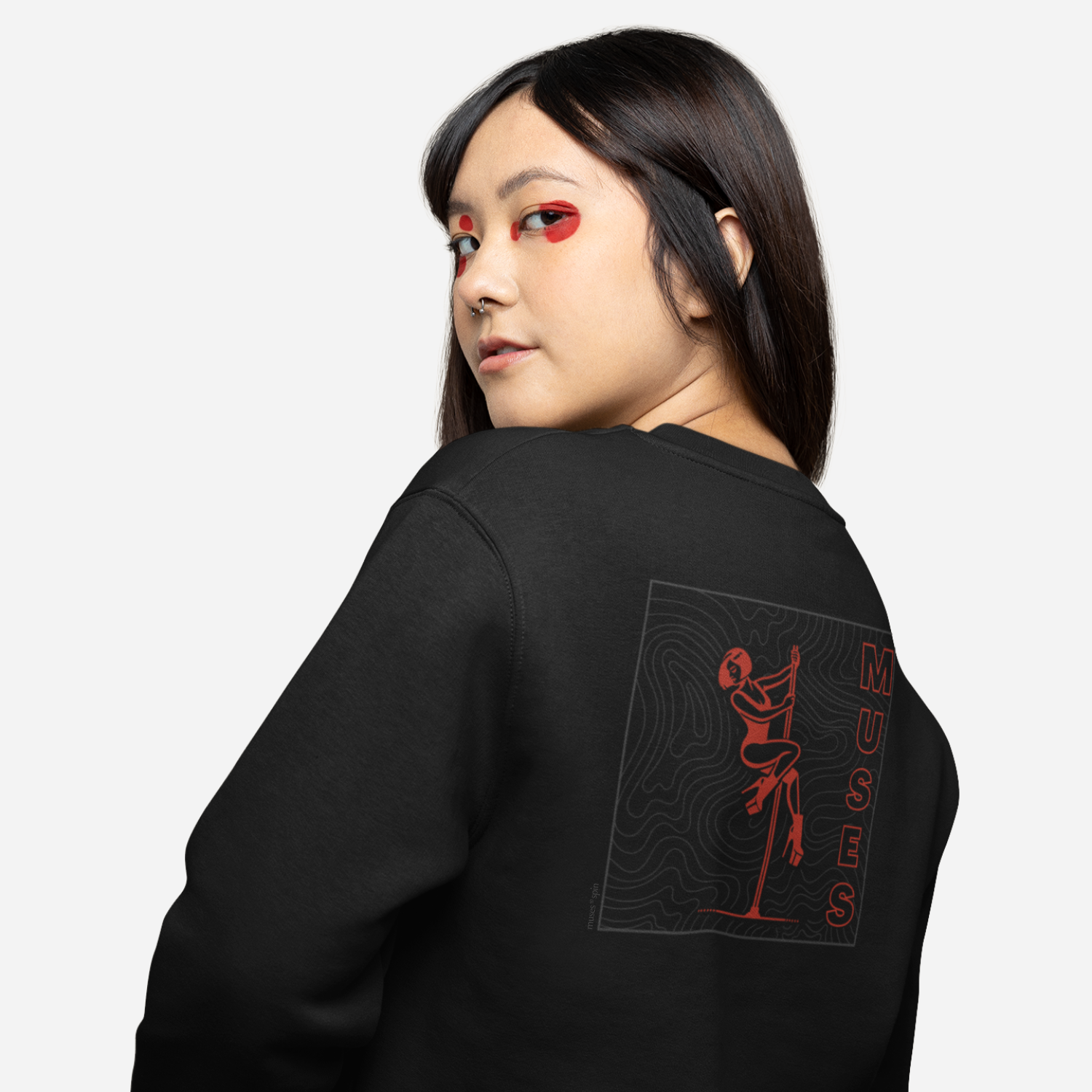 Woman in front of a white background wearing a black sweater with a dark red and grey design of a pole dancer and the word "Muses" on the side.