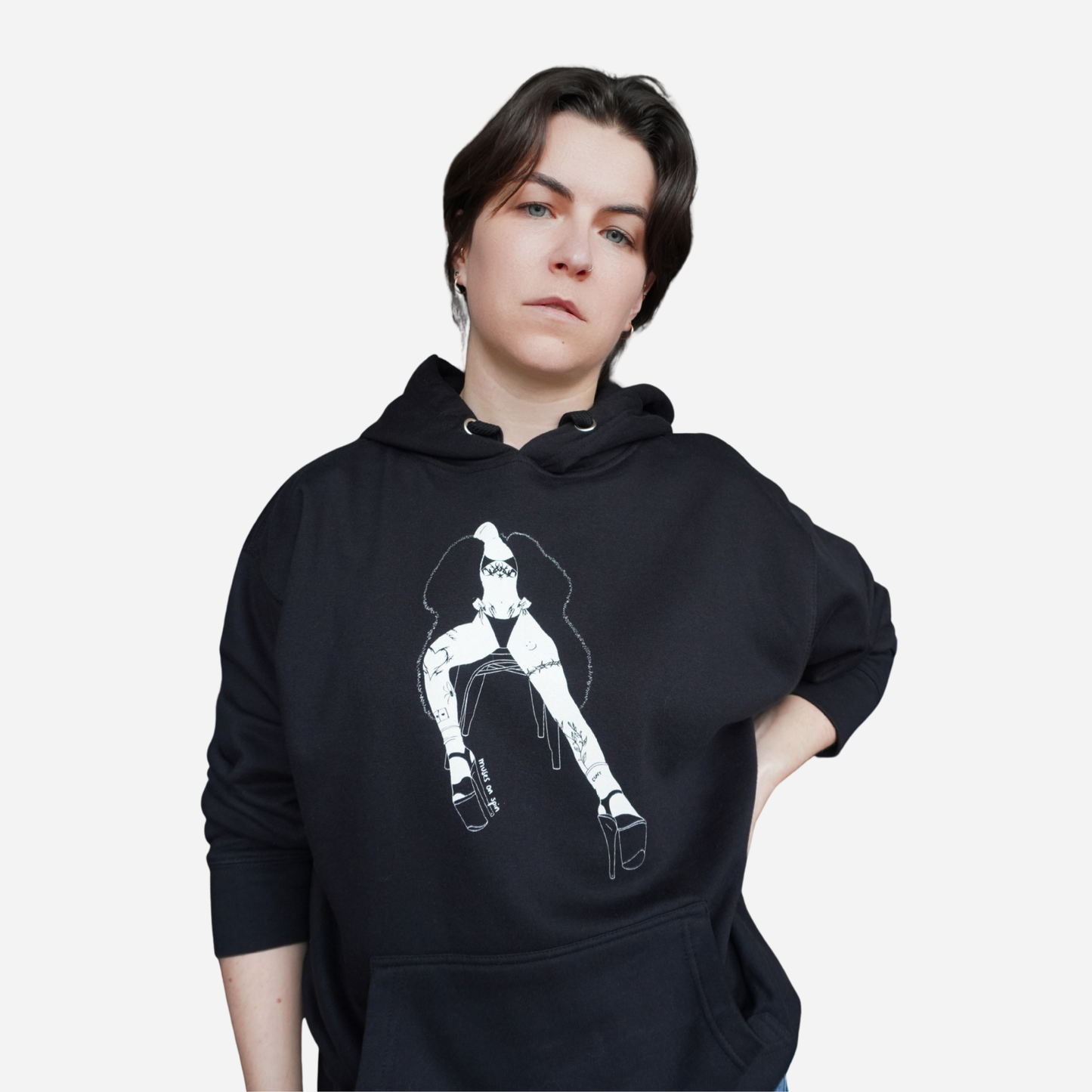 Person wearing a black hoodie with a white graphic design of a woman sitting on a chair, wearing a bikini and a large fluffy coat, on a white background
