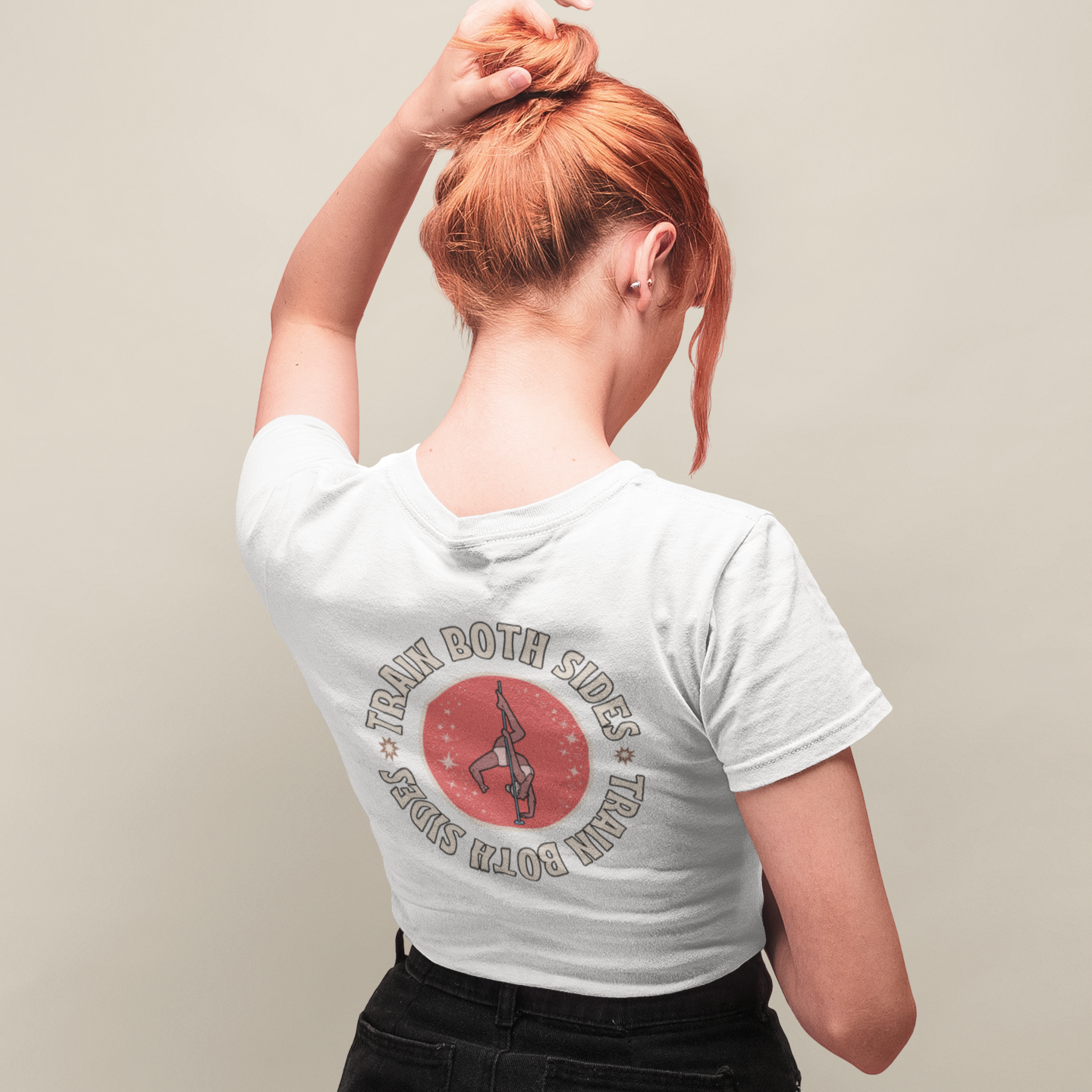 Woman facing away , standing in front of an off-white background. She is wearing a white tshirt with a graphic stating "Train Both Sides".