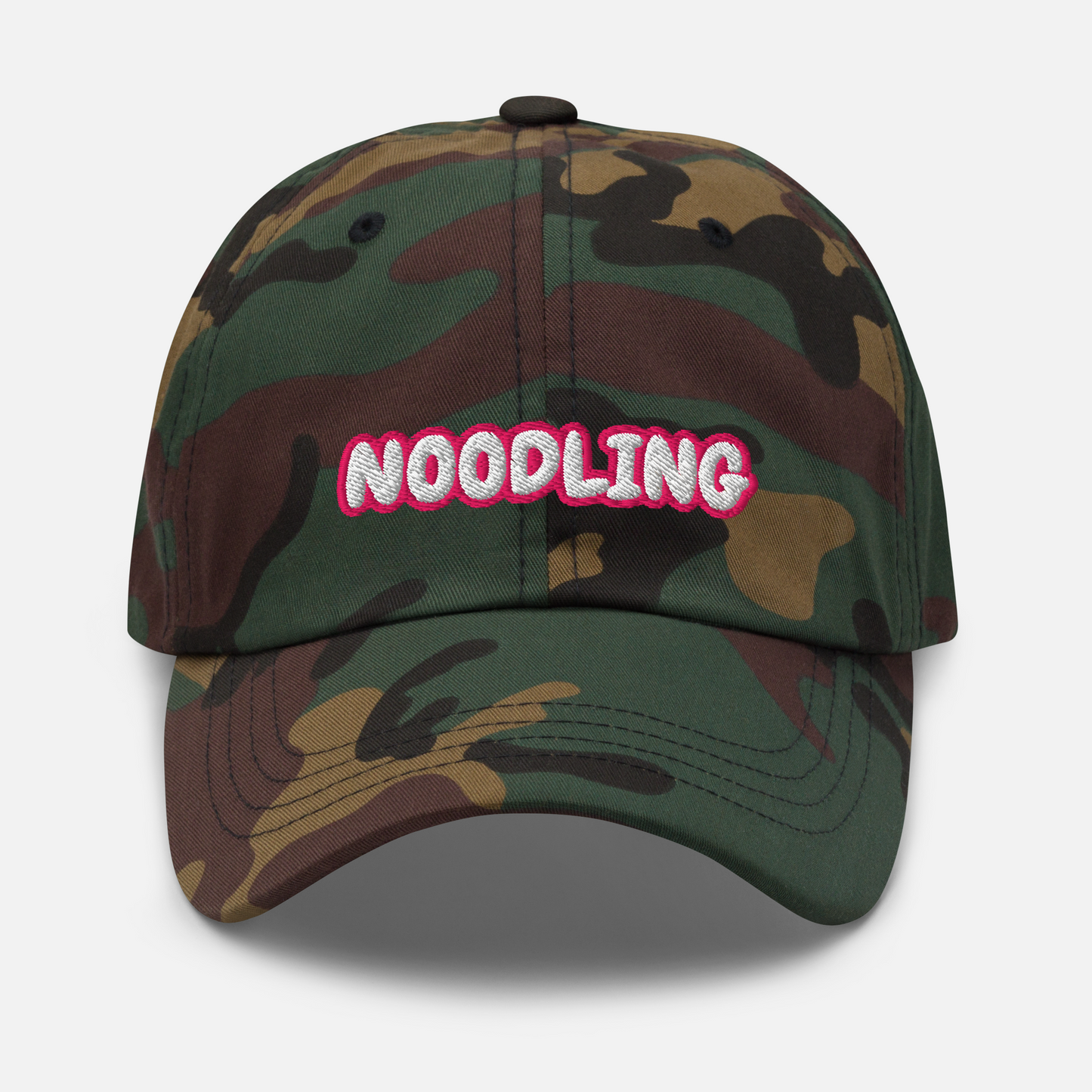 Camo-coloured cap in front of a white background. The word "Noodling" is embroidered in white letters with a pink outline on the front of the cap.